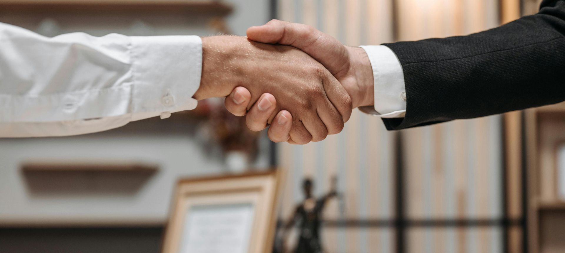 Close-up of a handshake between two professionals in a modern office setting, emphasizing partnership and agreement.